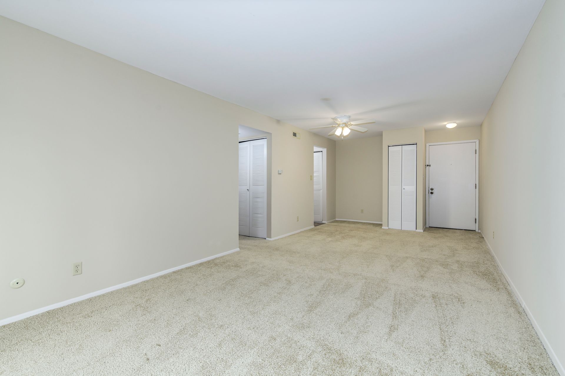 Empty room with beige carpet and walls, three doorways, and a ceiling fan.