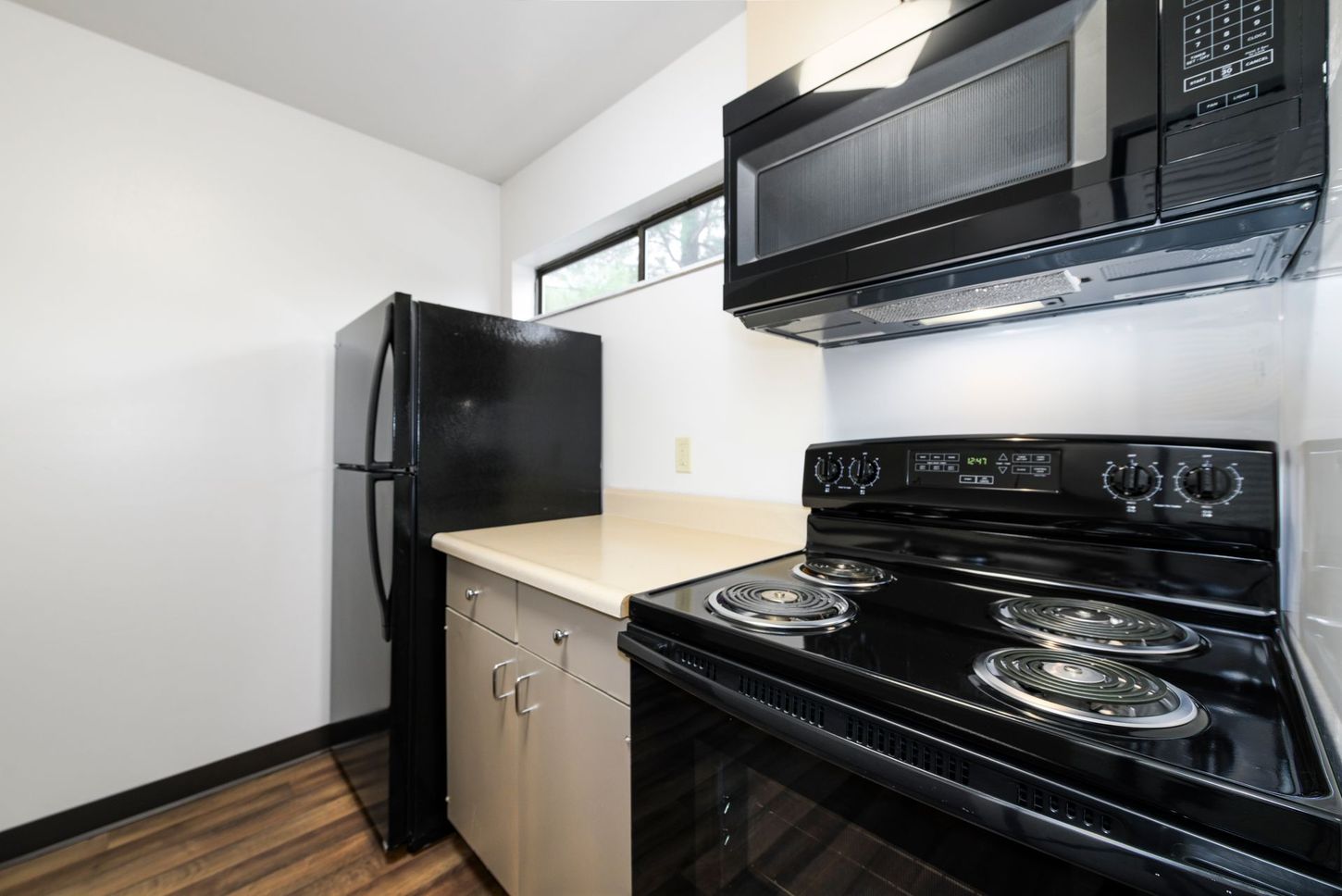 Black kitchen appliances including fridge, microwave, and stove in a small kitchen. Beige countertop and cabinets.