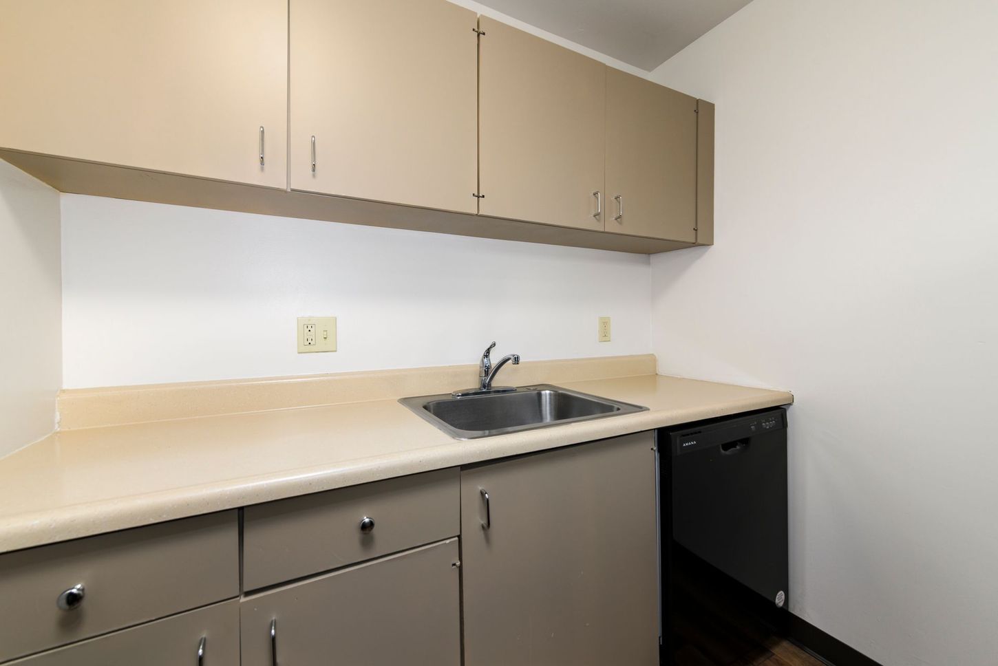 Beige kitchenette with upper and lower cabinets, sink, and dishwasher.