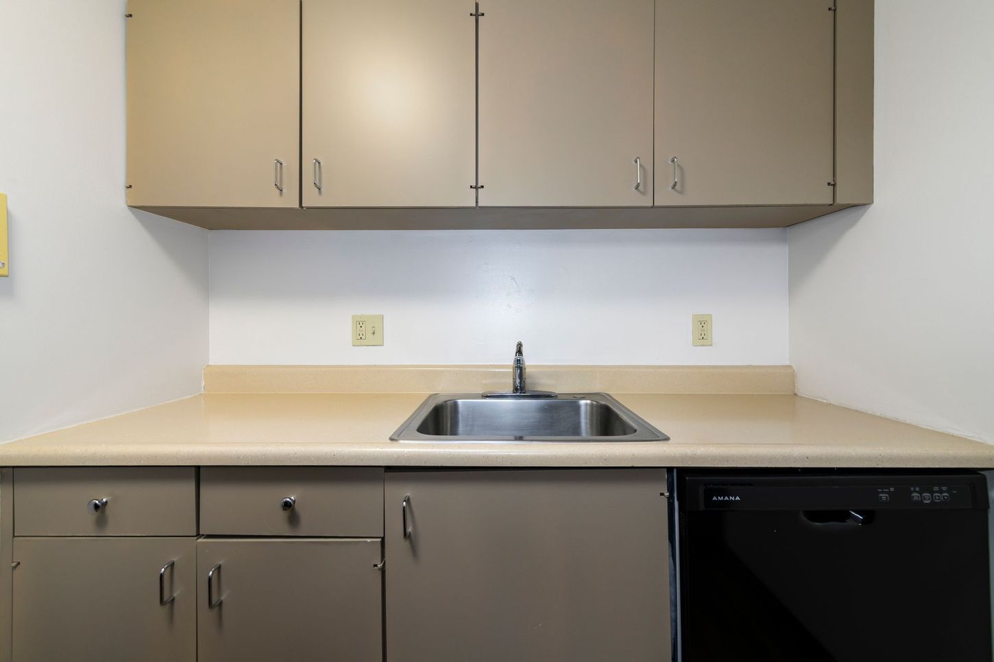 Kitchen with upper and lower beige cabinets, stainless steel sink, and black dishwasher.