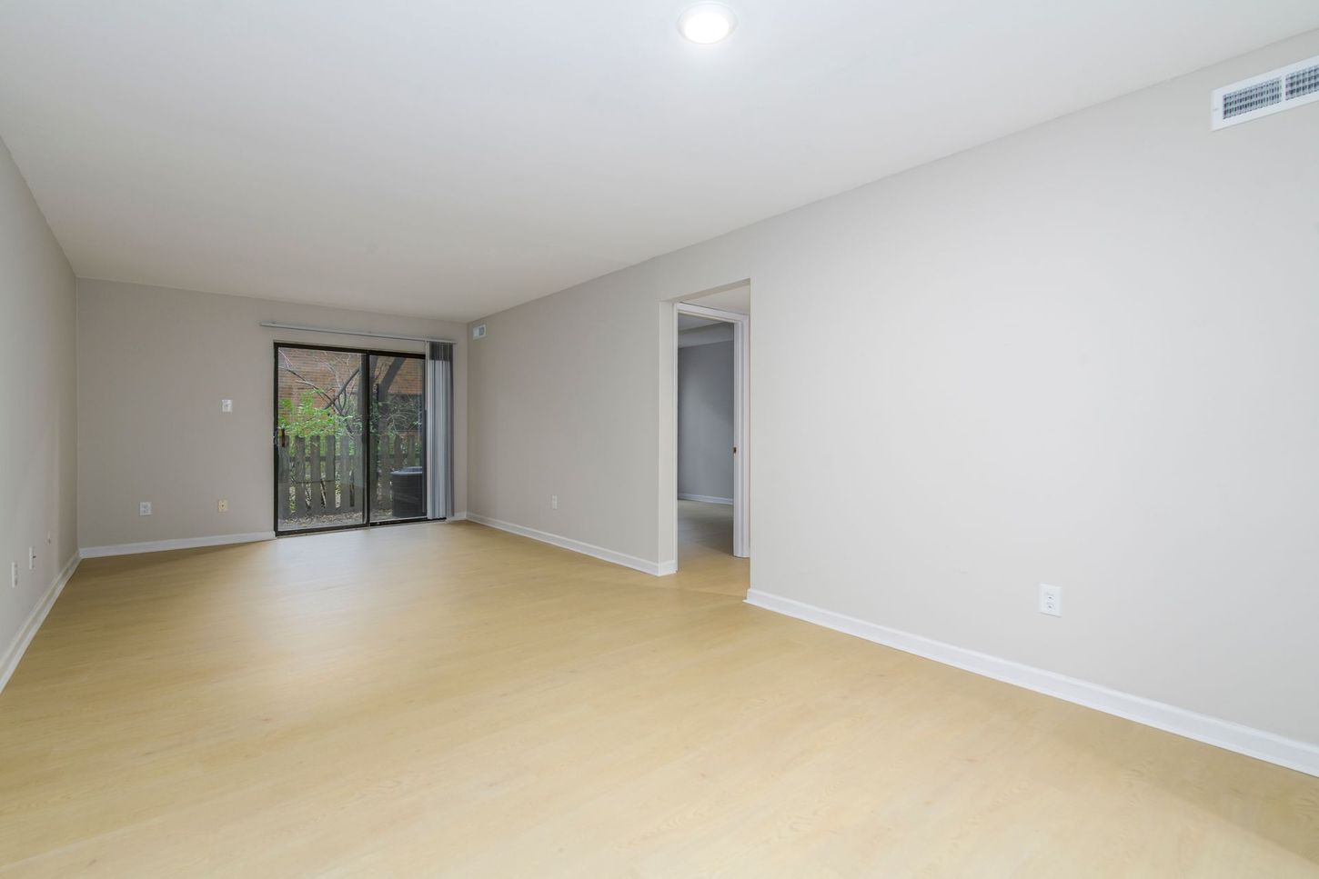 Empty room with light-colored flooring, neutral walls, sliding glass door, and a doorway.