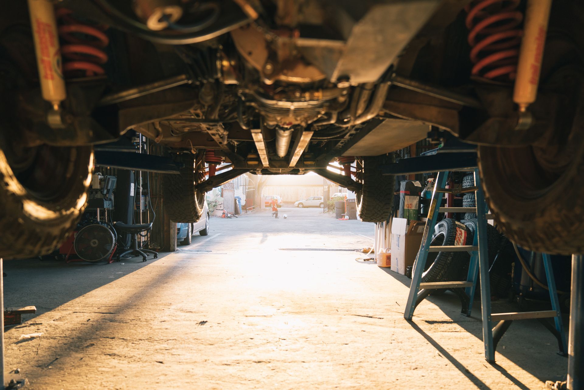 Undercarriage of a car on a lift in a garage, with sunlight streaming in from the open bay
