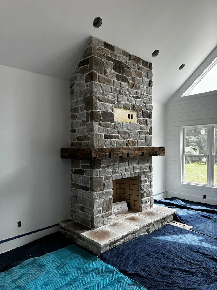 Stone fireplace in a bright living room with a large window and blue floor covering during renovation