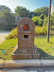 Brick mailbox on a curb with an arched red opening in a sunny suburban yard