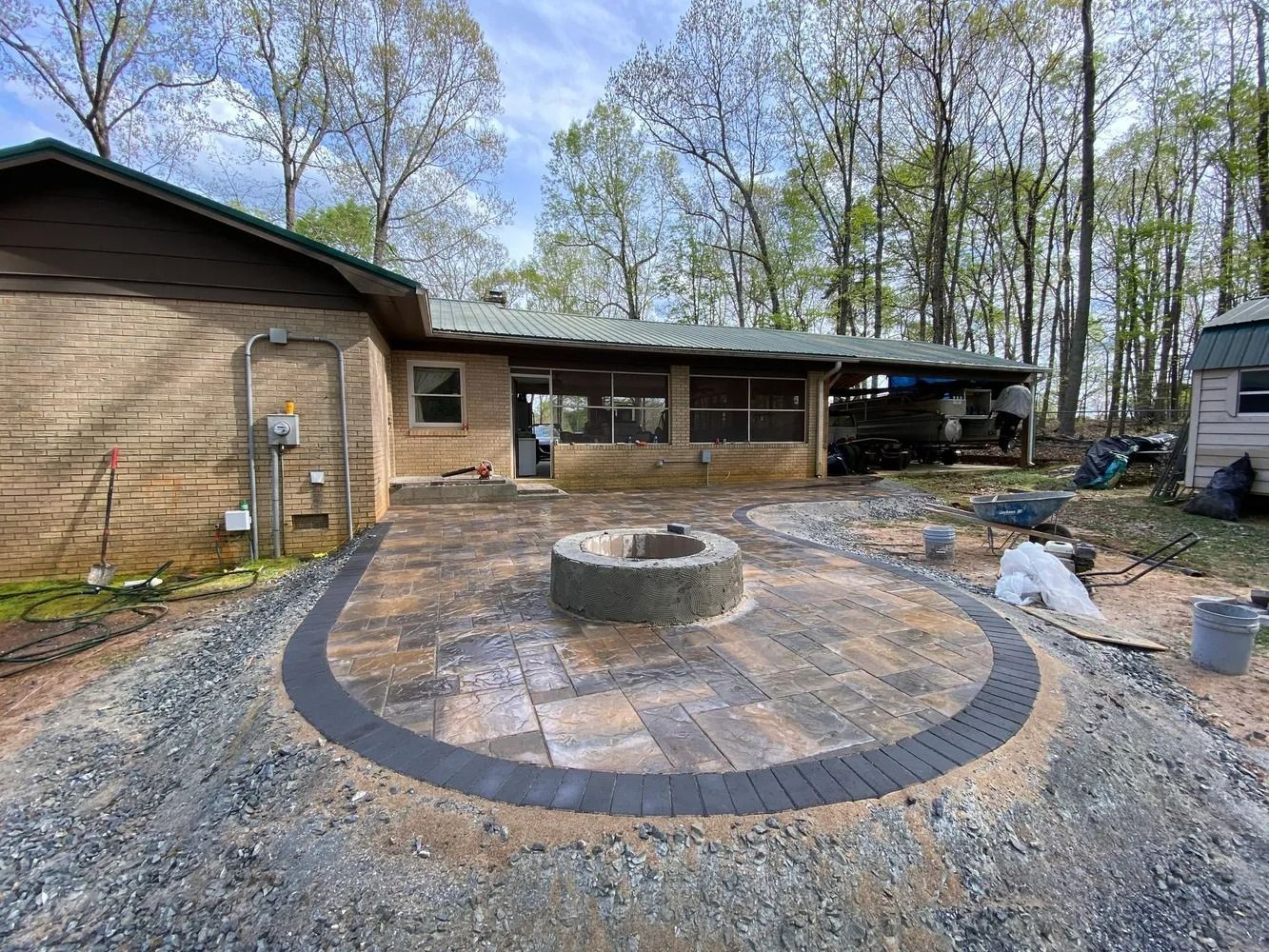 Backyard patio with a circular stone fire pit, paved seating area, and wooded house exterior.