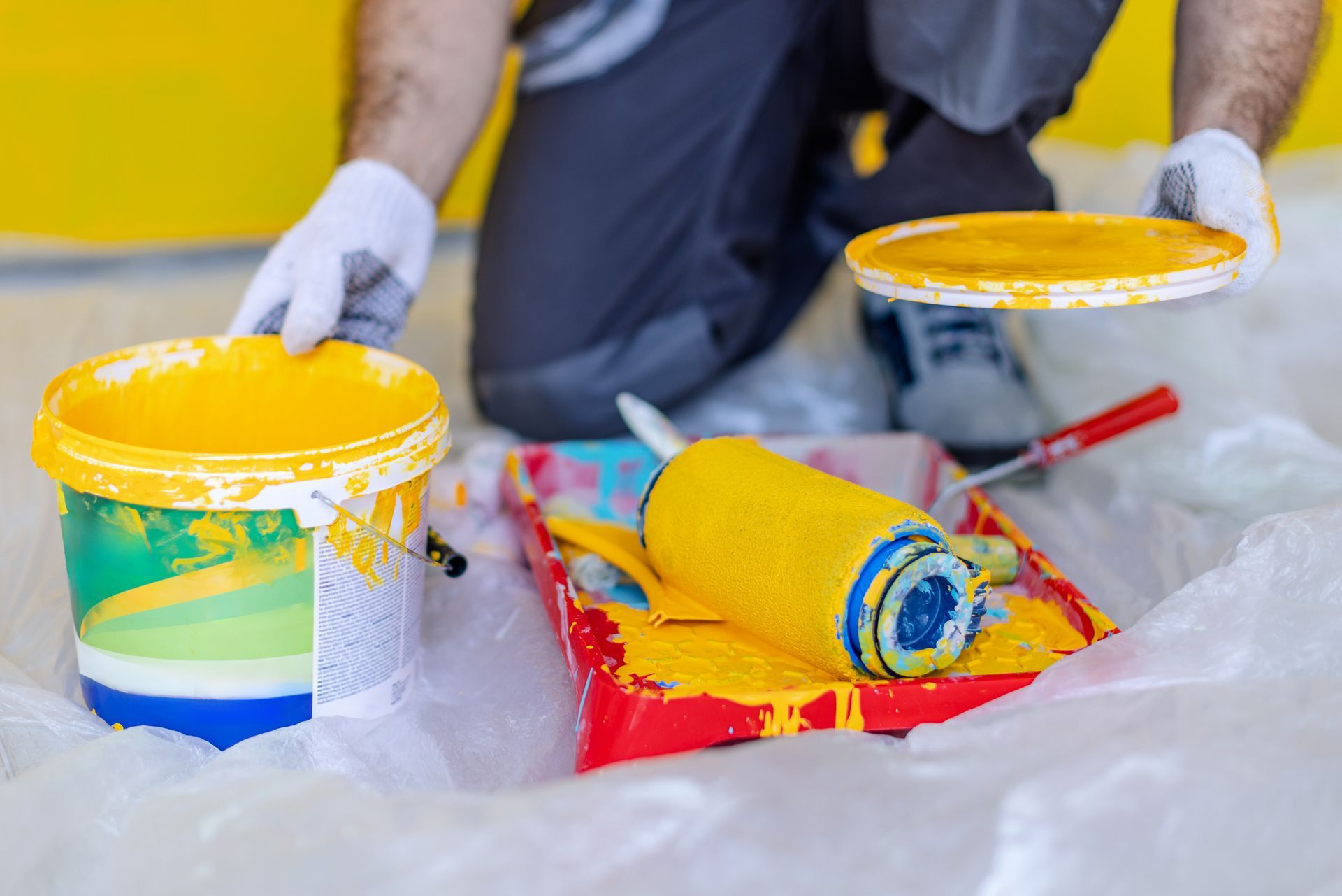 Commercial painter at work applying vibrant yellow paint on interior wall with supplies.