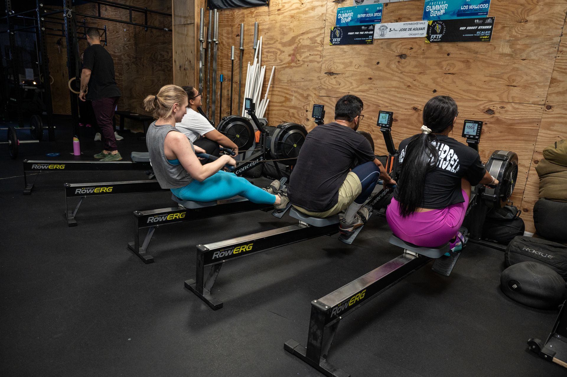 A group of people are sitting on rowing machines in a gym.