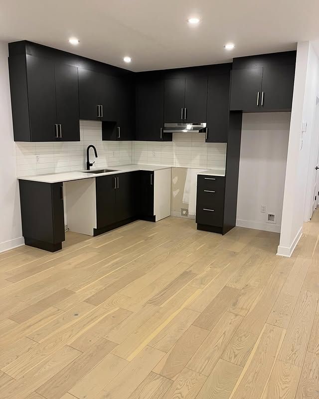 Cuisine moderne avec armoires noires, crédence blanche, parquet clair et robinet noir.