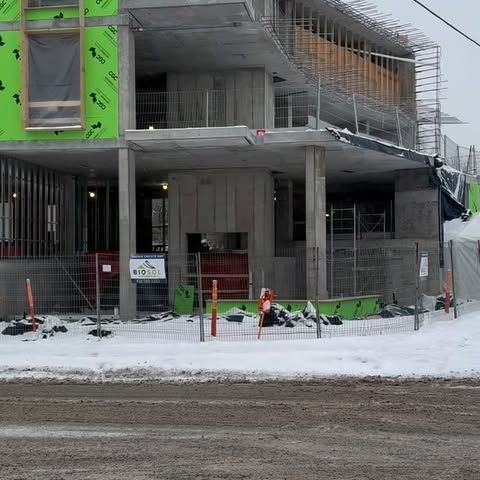 Chantier de construction avec un bâtiment en béton partiellement érigé par temps de neige. L'isolant vert est visible.