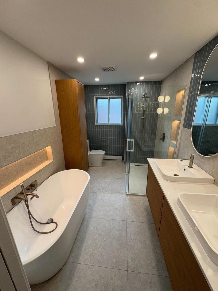 Salle de bains moderne avec baignoire, douche, double vasque et meubles en bois. Dominée par les tons gris et blancs.
