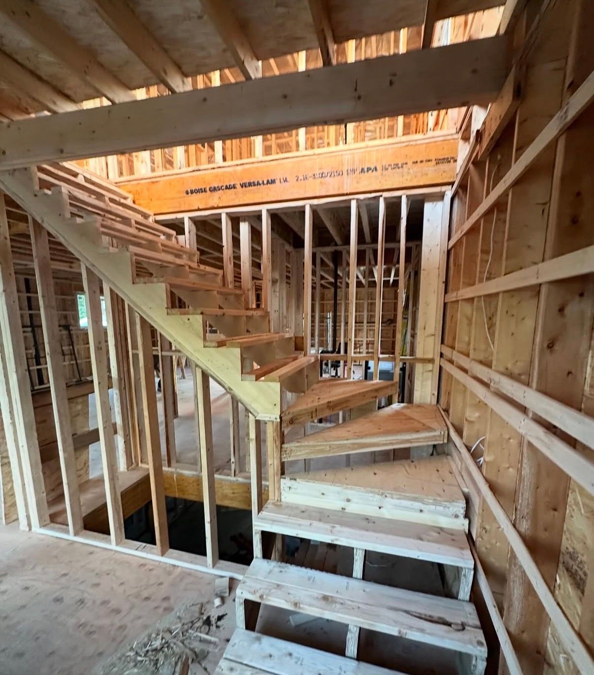 Vue intérieure d'un escalier en bois en construction. La charpente et les marches en bois sont visibles.