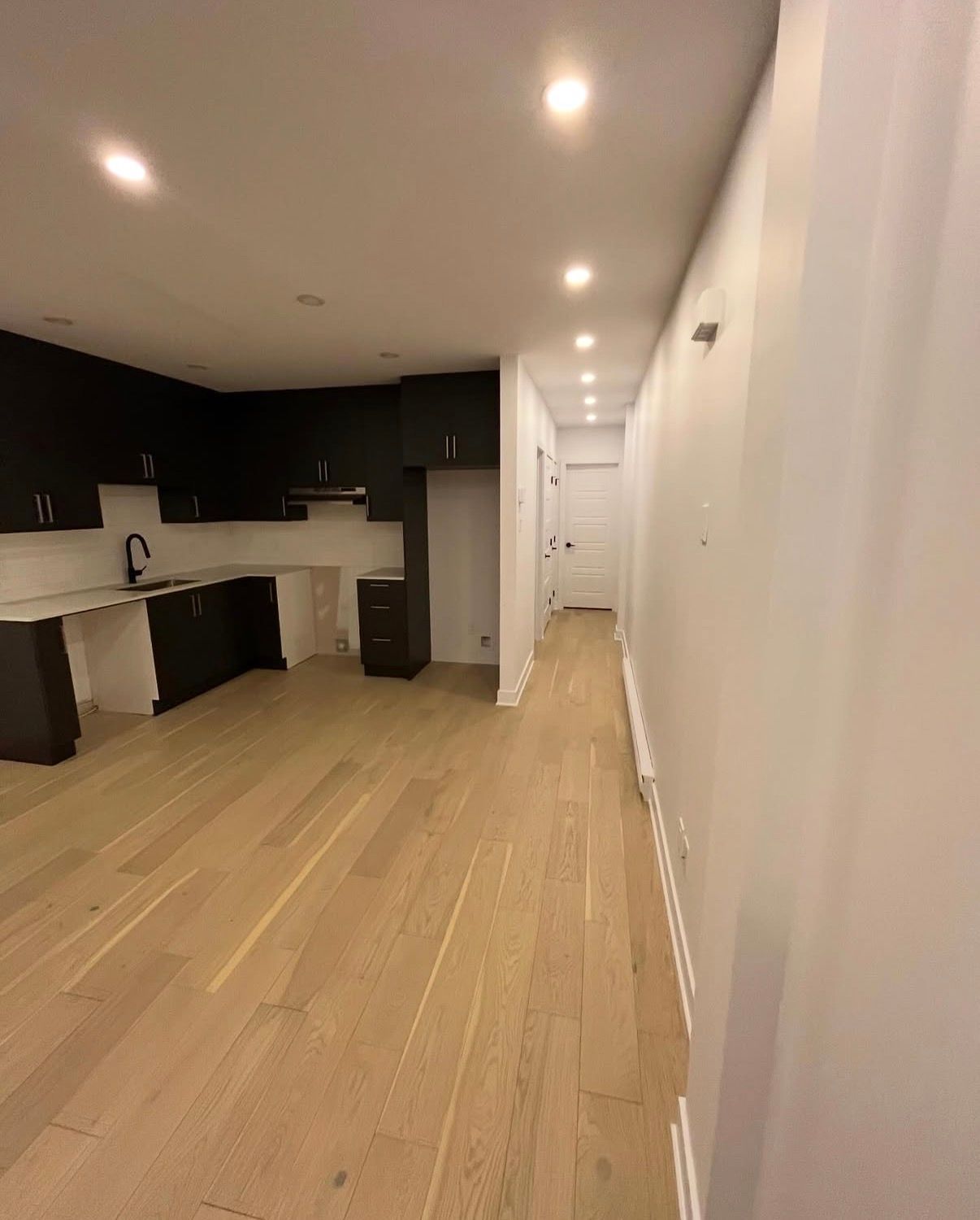 Cuisine moderne vide avec placards foncés, parquet clair et murs blancs.