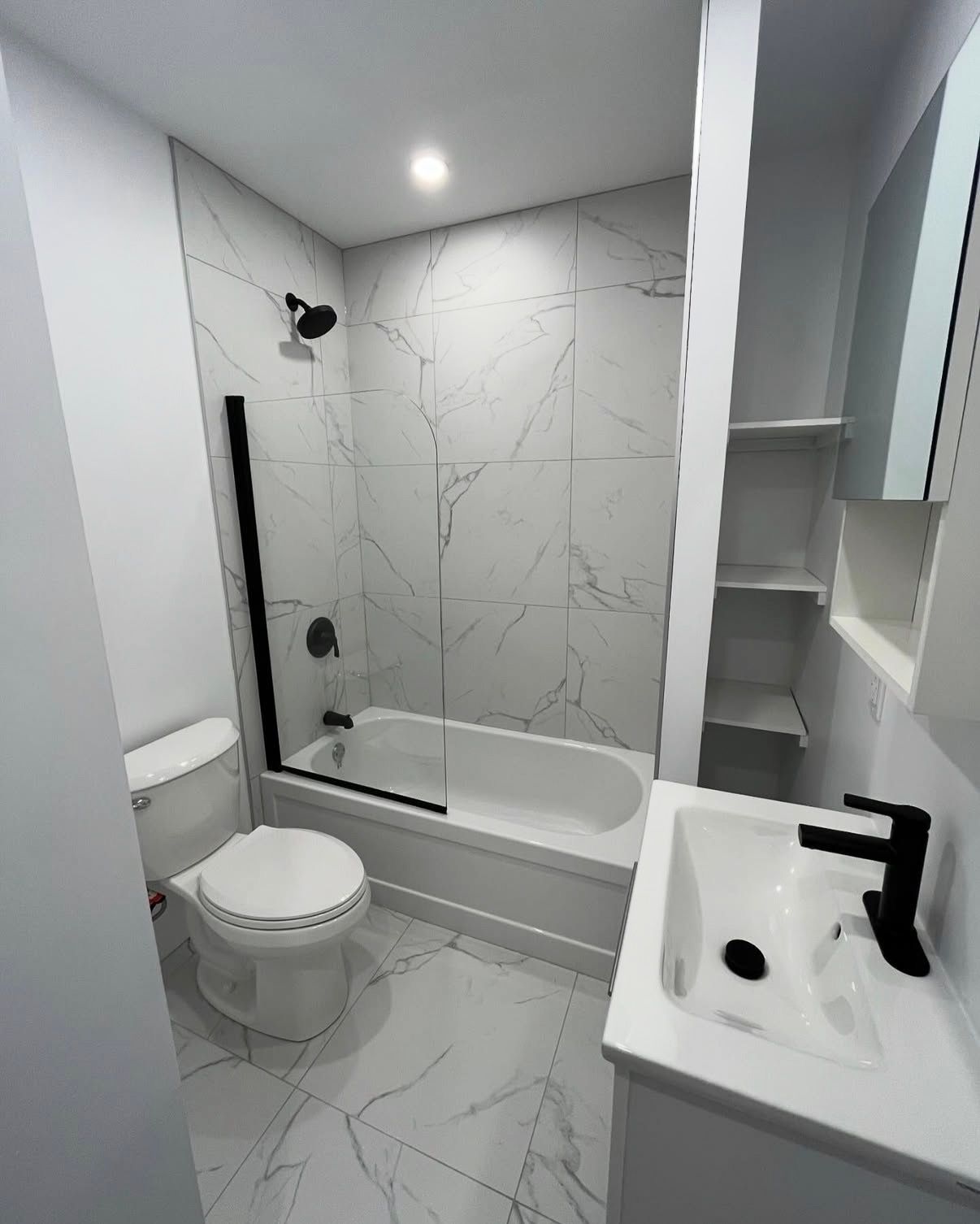 Salle de bains moderne avec carrelage en marbre blanc, robinetterie noire et meuble-lavabo blanc.