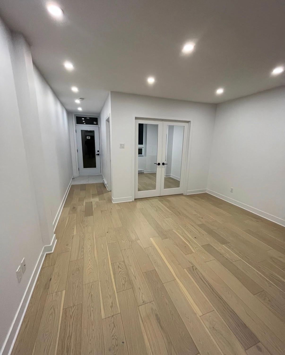 Pièce vide avec parquet clair, murs blancs et éclairage encastré.
