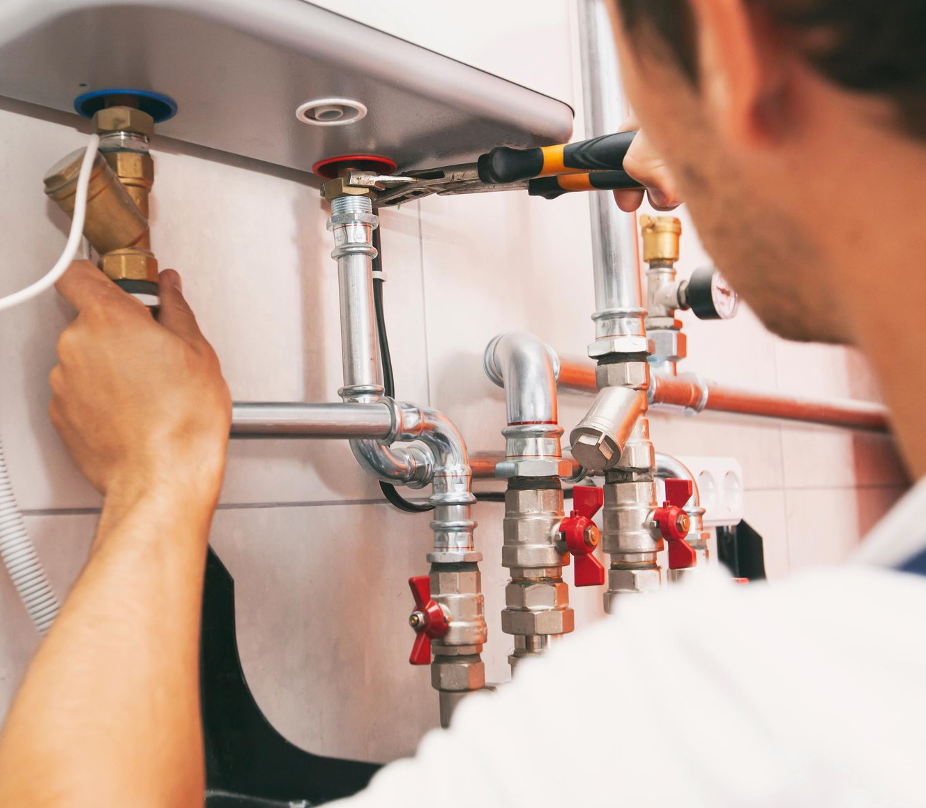 A technician adjusting water heater valves and connections during maintenance work.