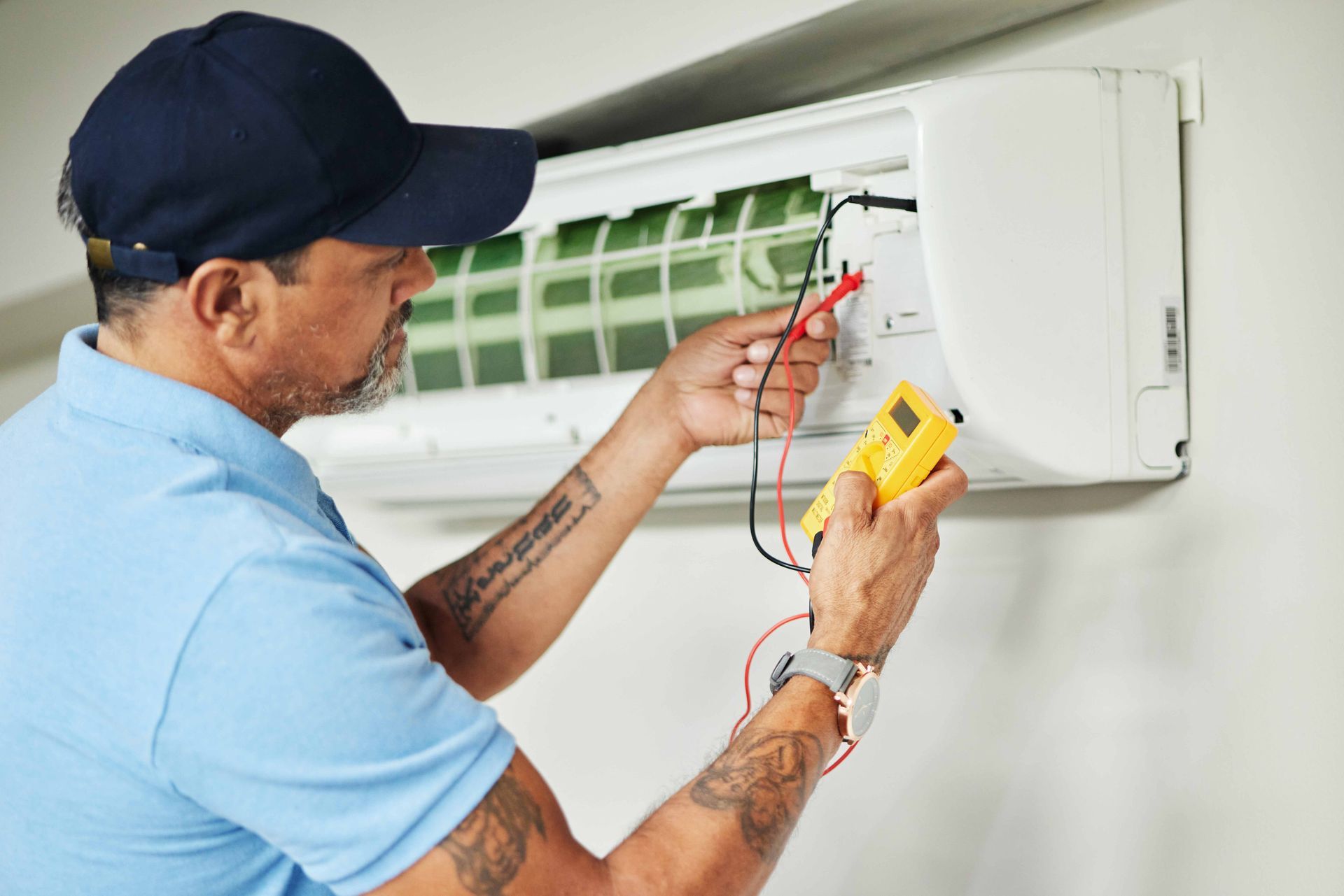 A technician using a multimeter to test wiring on a wall-mounted air conditioner during repair work