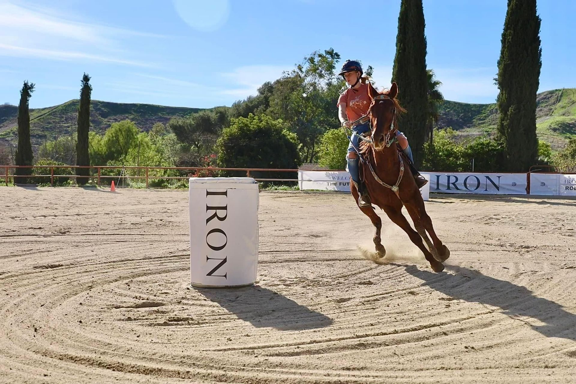 Rider participating in local barrel racing event demonstrating tight turn around barrel on outdoor arena
