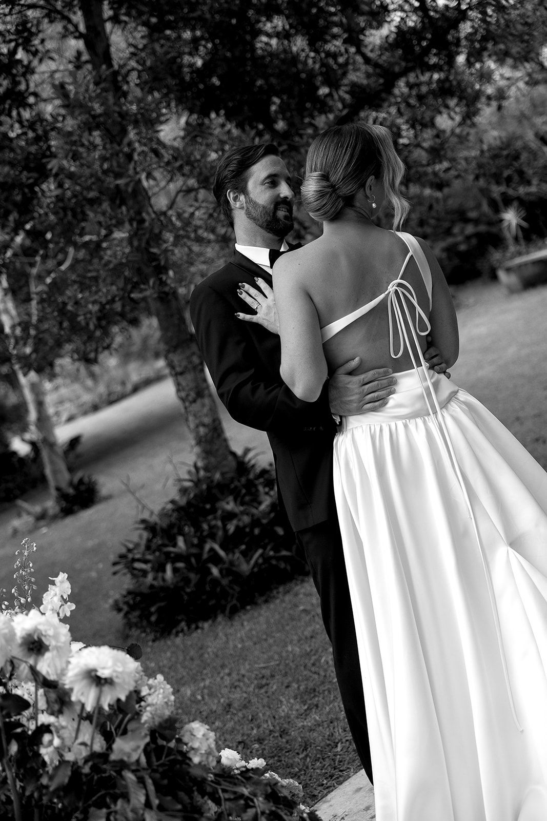A black and white photo of a bride and groom dancing in a park.