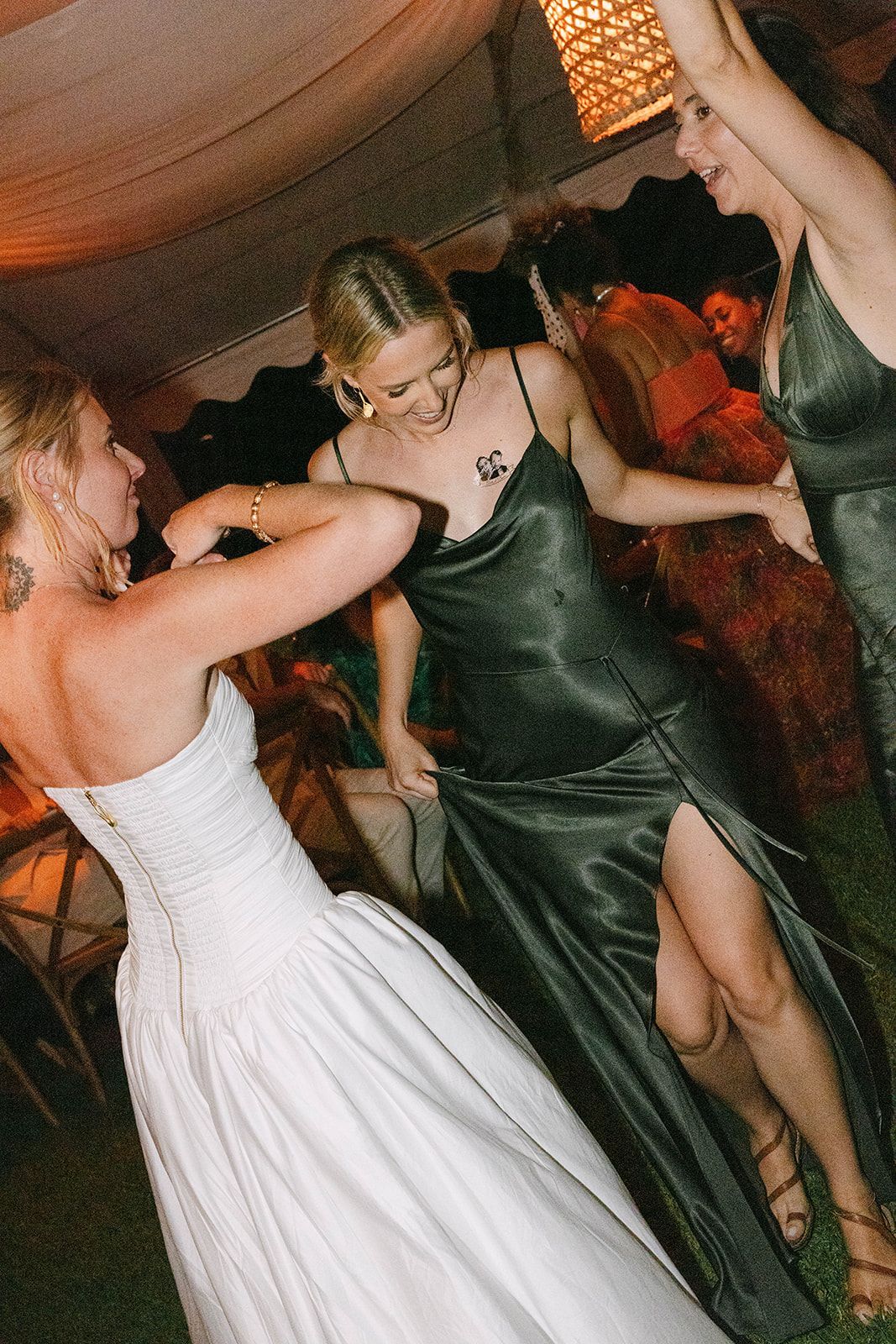 A woman in a white dress is dancing with two other women in green dresses.