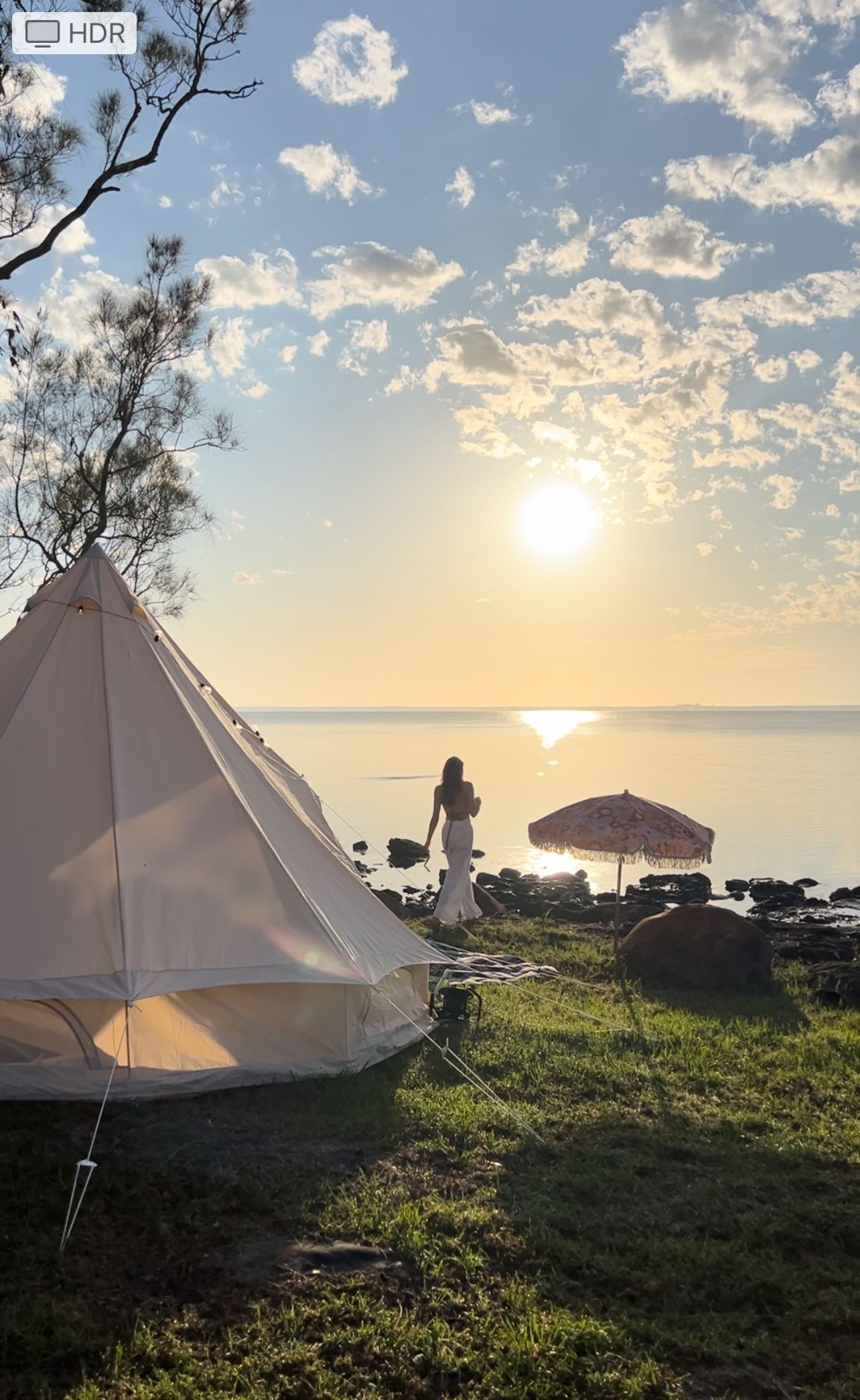 A woman is standing in front of a tent on a beach at sunset.