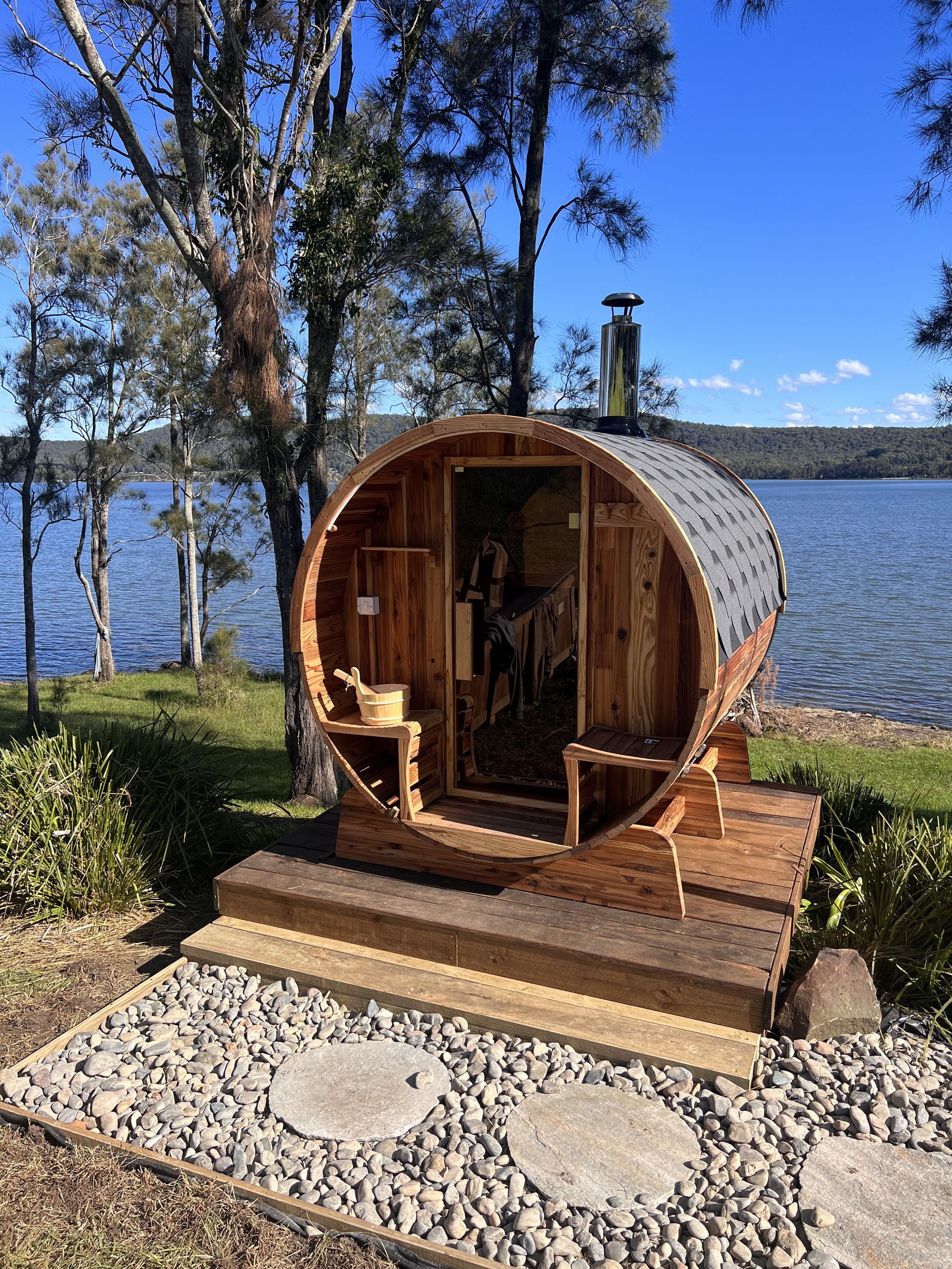A wooden barrel sauna is sitting next to a lake.