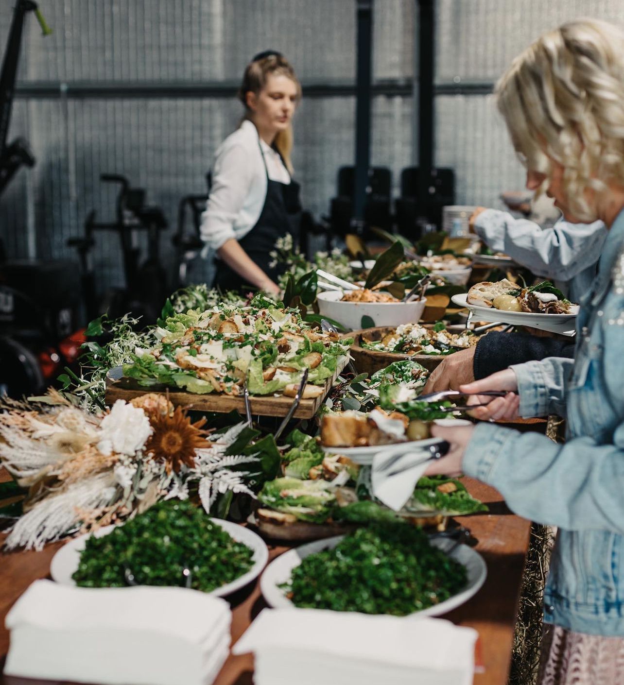 A group of people are standing around a table full of food.