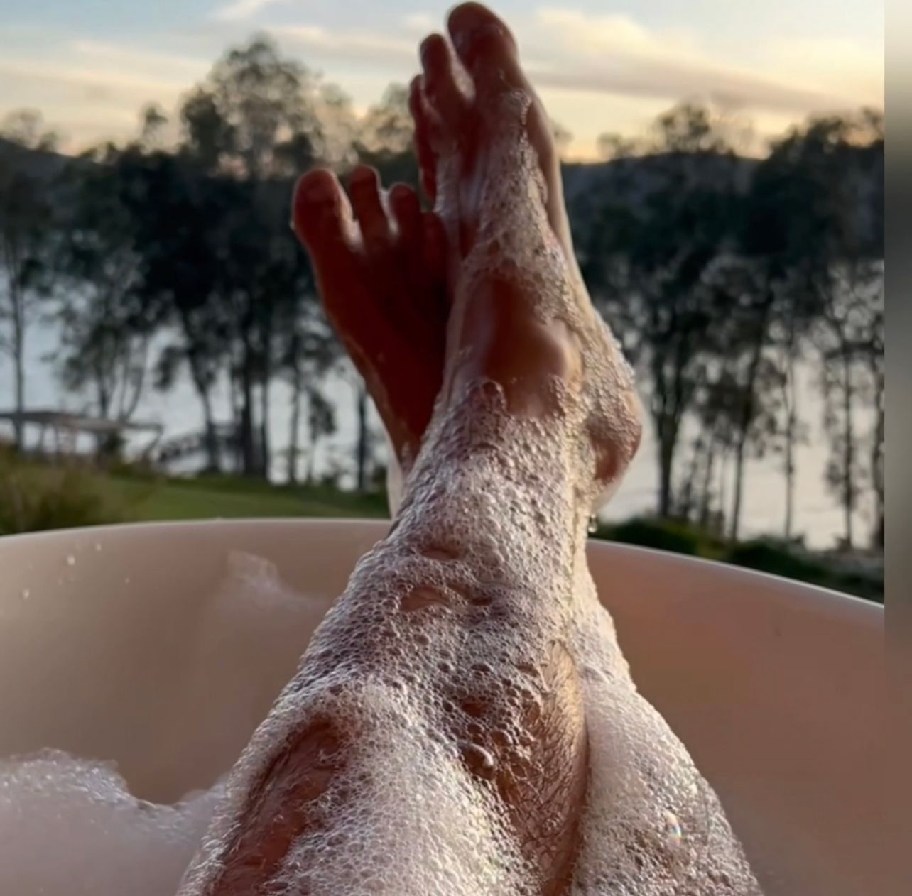 A person is taking a bath with their feet in the water.