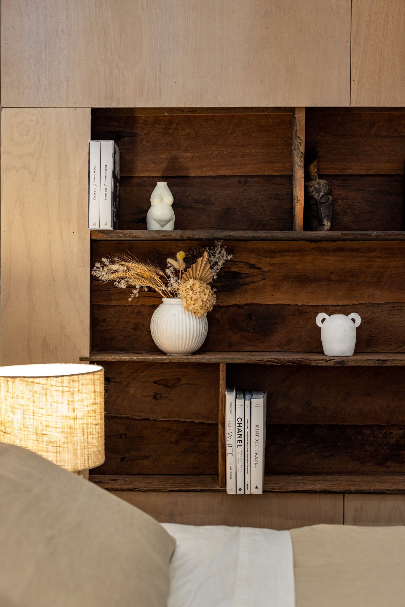 A wooden shelf with a vase of flowers on it in a bedroom.