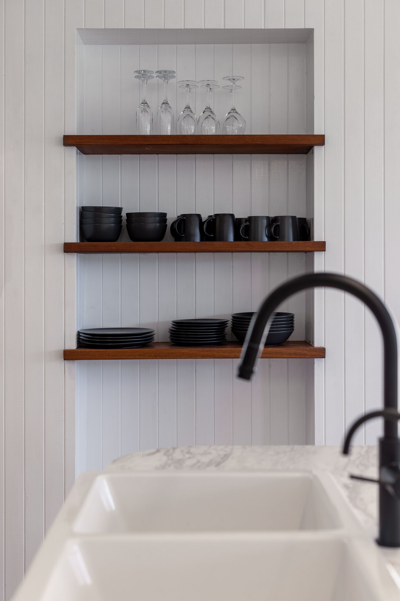 A kitchen sink with a black faucet and shelves filled with bowls and glasses.