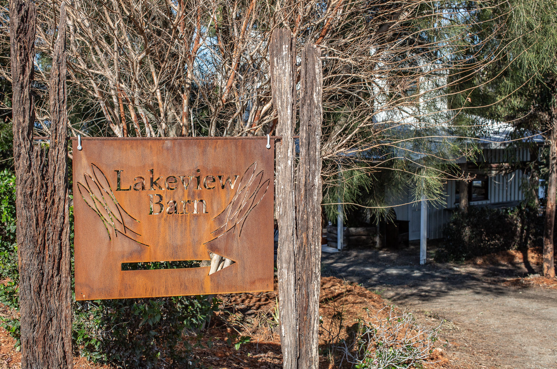 A rusty sign is hanging from a tree in front of a house.