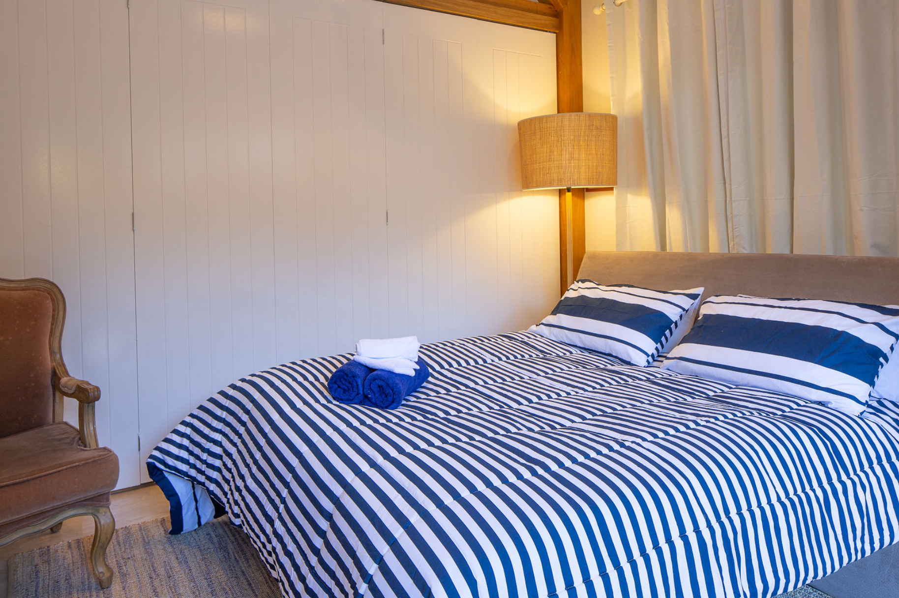 A bedroom with a bed , chair and lamp . the bed has a blue and white striped comforter.