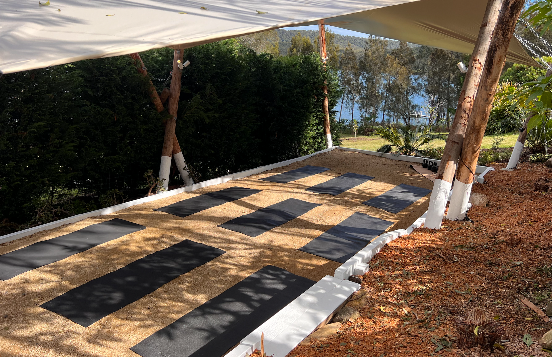 There are many yoga mats on the ground under a canopy.