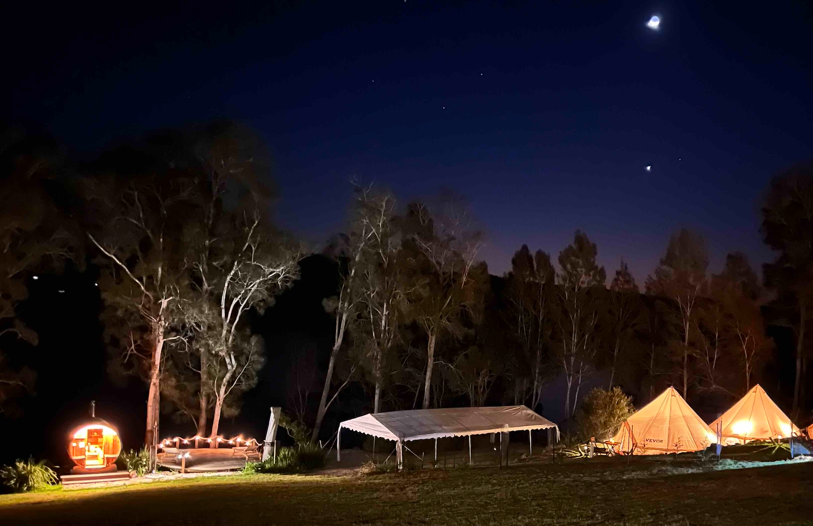 A group of tents are lit up in a field at night.