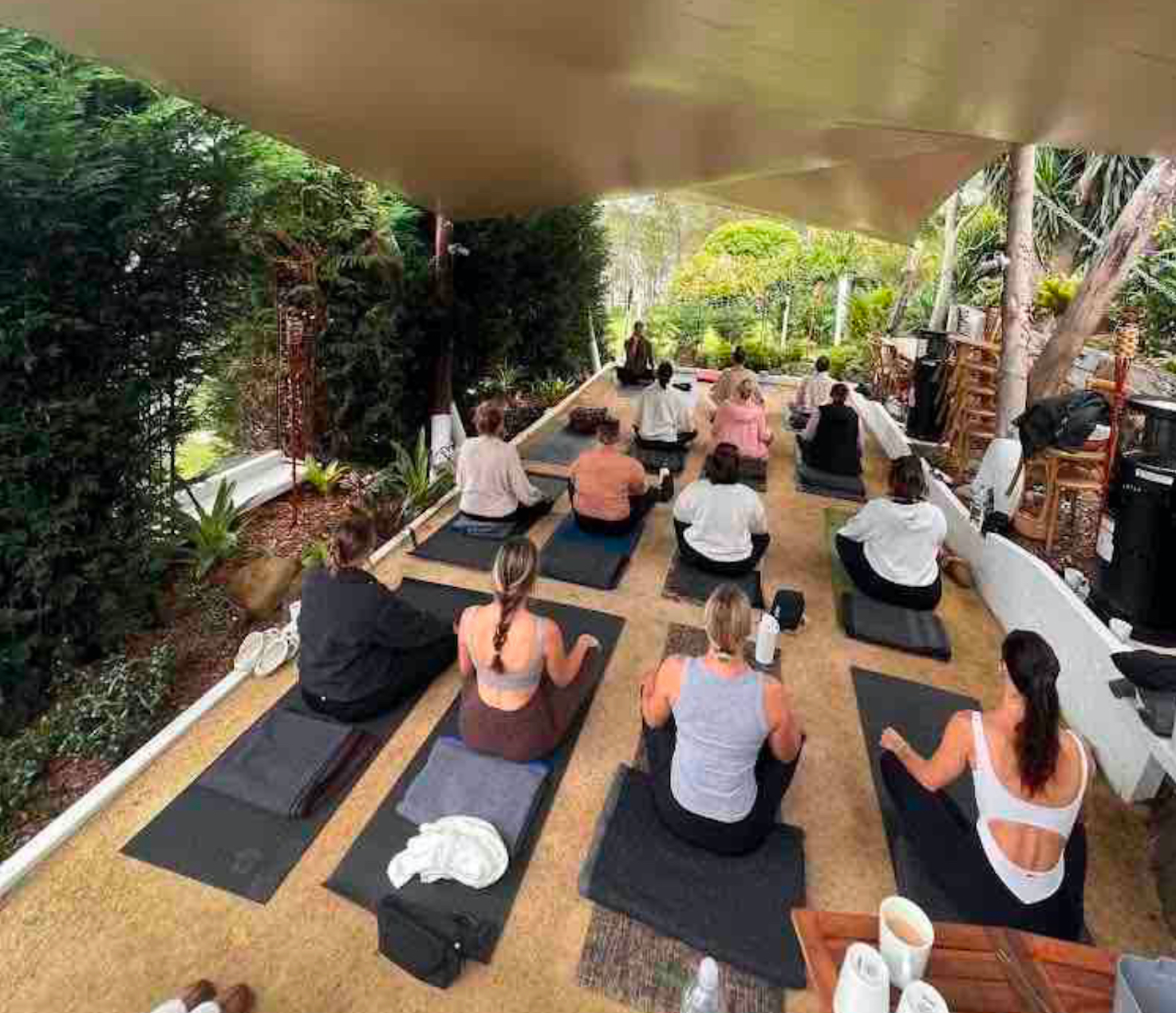 A group of people are sitting on yoga mats under a canopy.