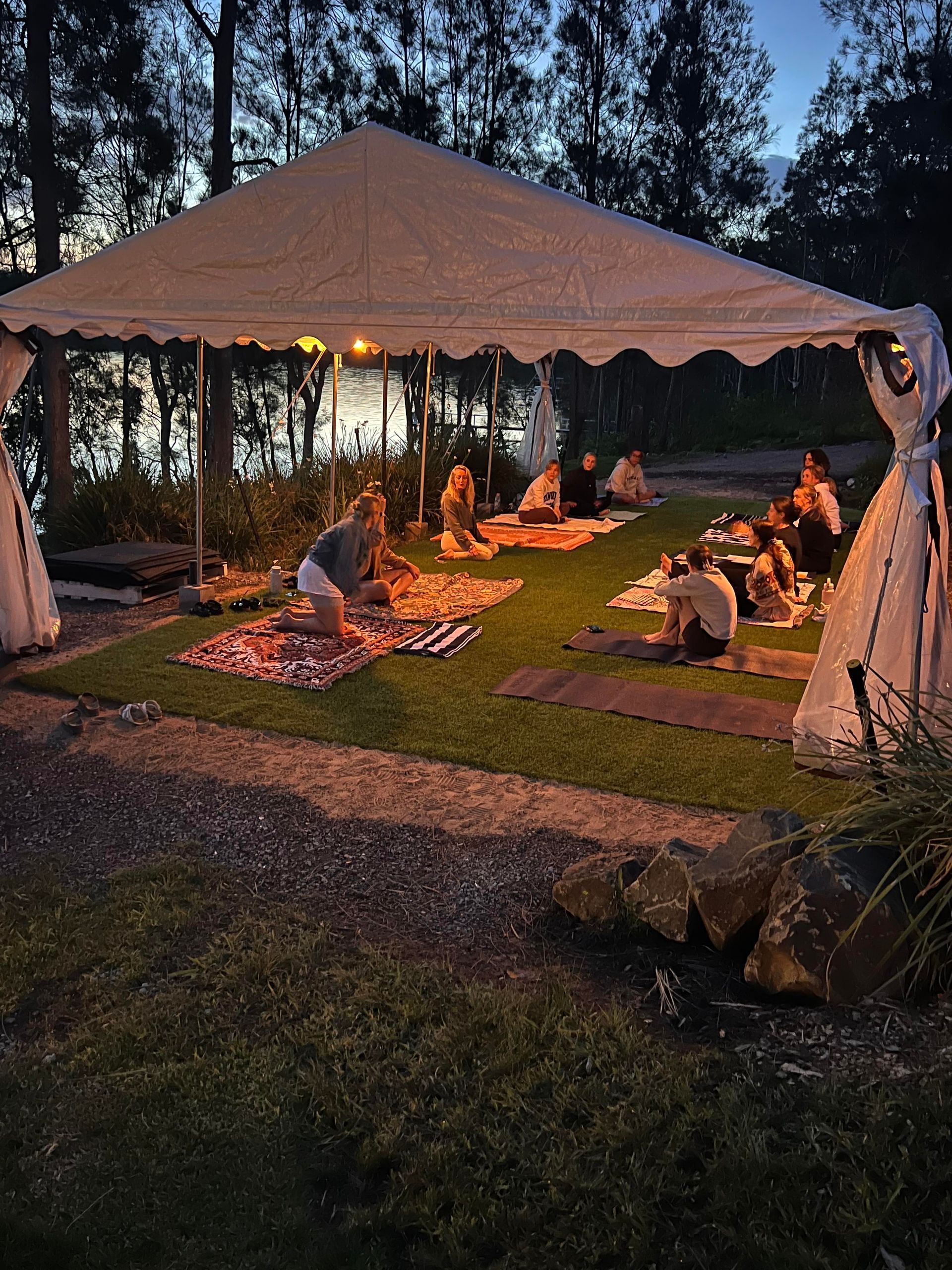 A group of people are sitting on yoga mats under a tent.
