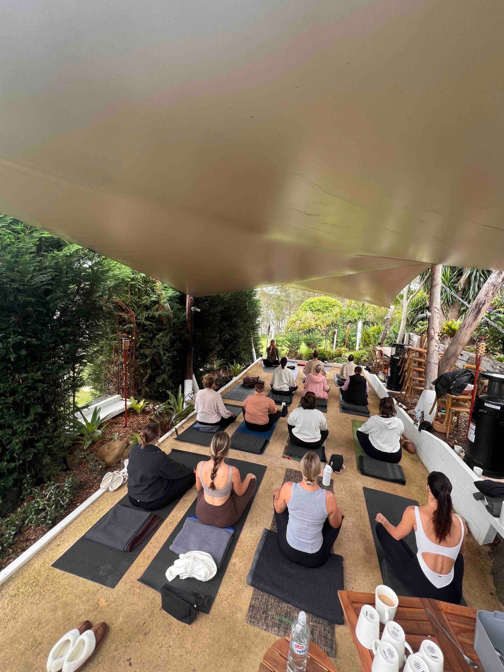 A group of people are sitting on yoga mats under a canopy.