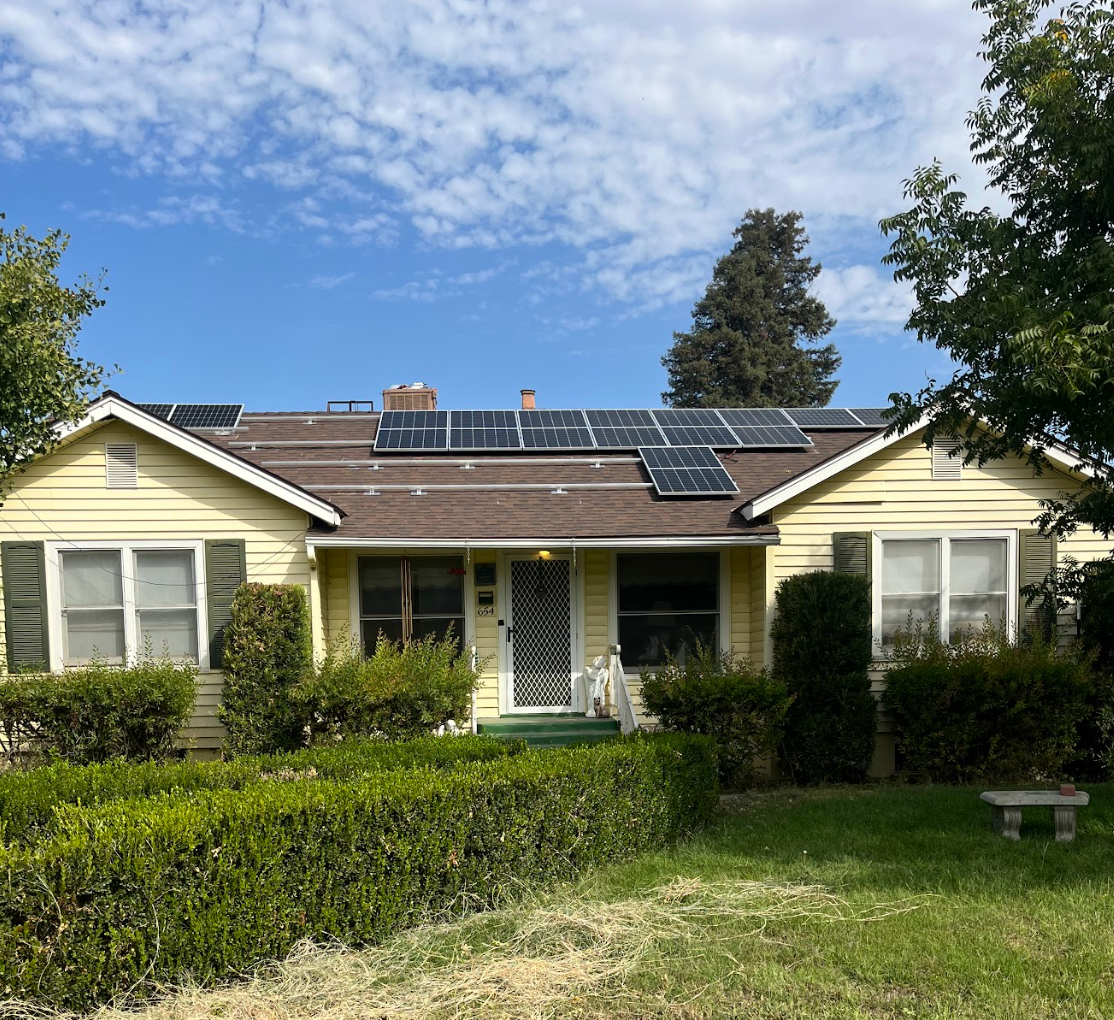 A technician in work clothes installs solar panels on a rooftop, securing the frame with their hands.