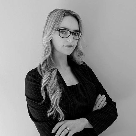 A black and white photo of a woman wearing glasses and a suit.