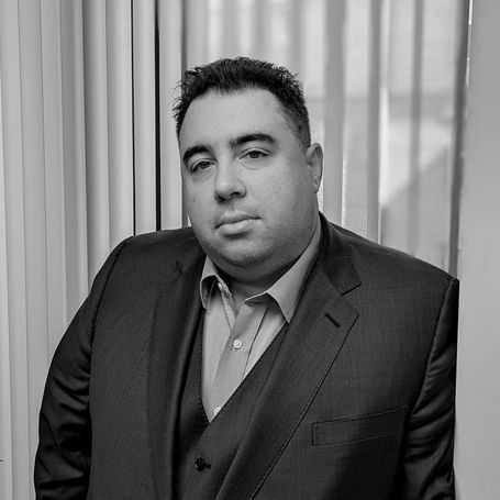 A man in a suit and vest is standing in front of a window.