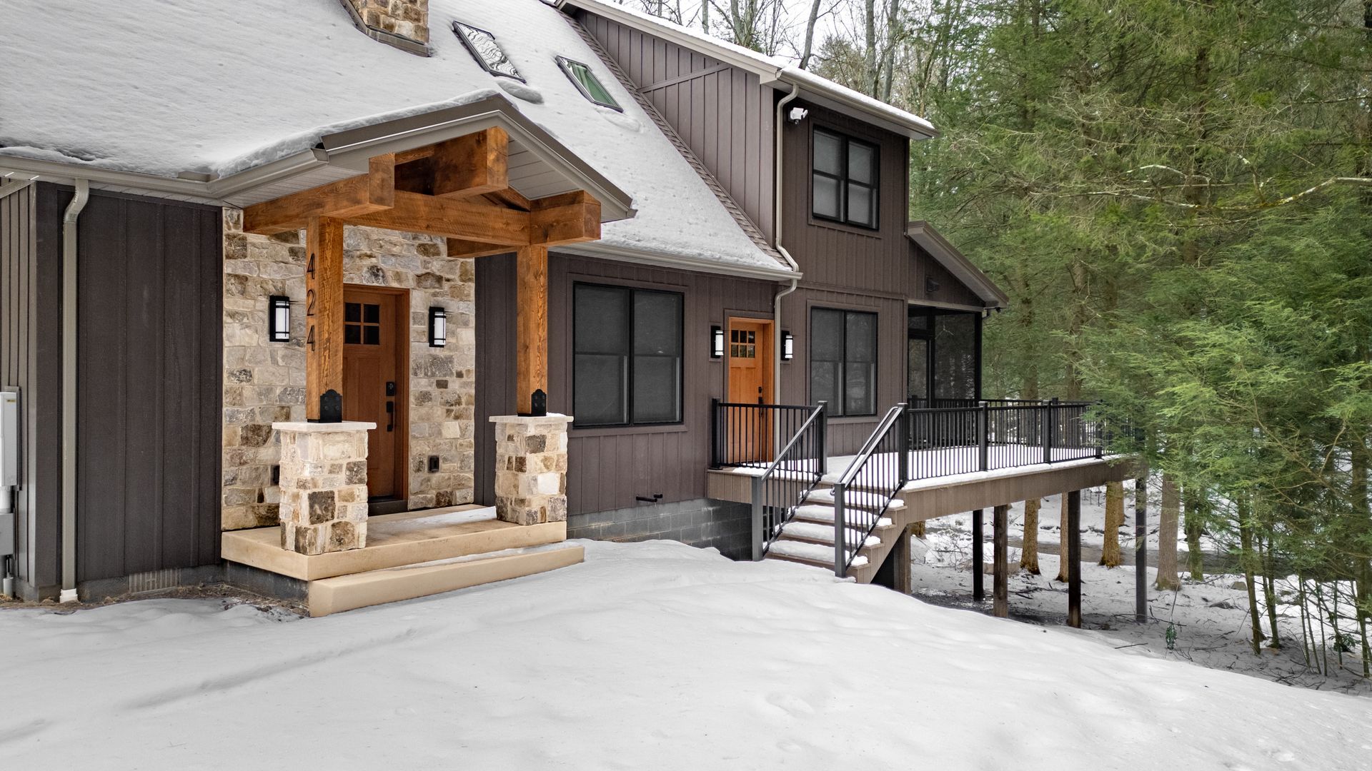 Snowy cabin entrance with wooden porch, lit windows, and a ramp leading to the door