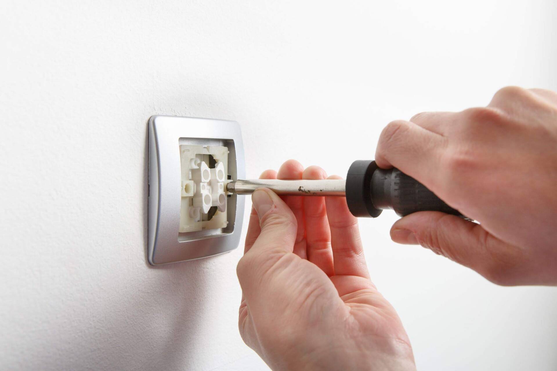 A person is fixing a light switch with a screwdriver.