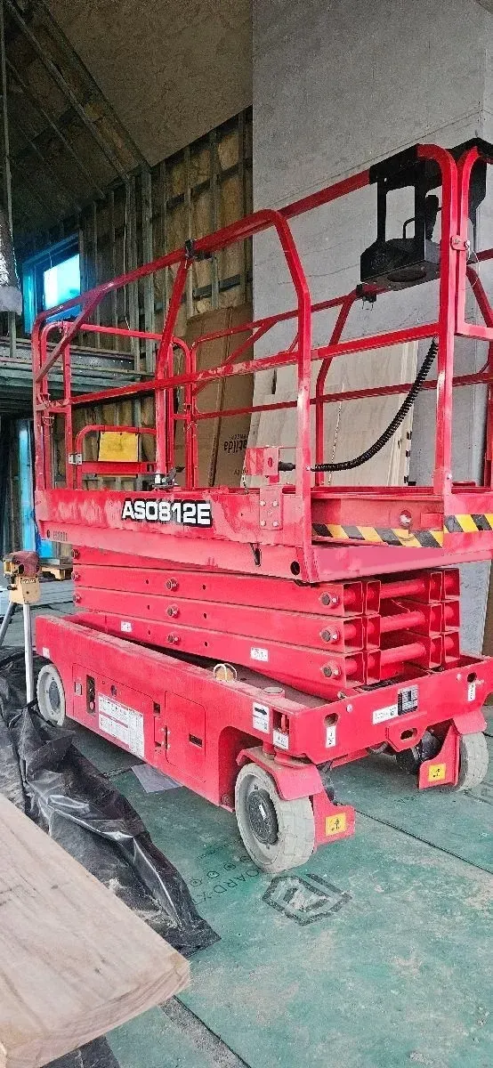 A Red Scissor Lift Is Parked in A Warehouse — PEPS Machinery Services In Logan, QLD