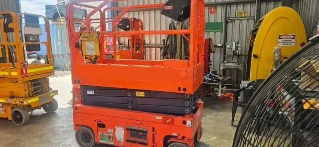 A Red Scissor Lift Is Parked in A Garage Next to A Fan — PEPS Machinery Services In Bethania, QLD