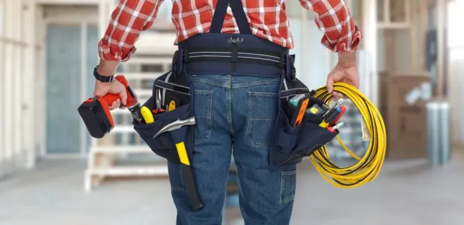 Close-up of an electrician's tool belt with drill and yellow electrical wire.