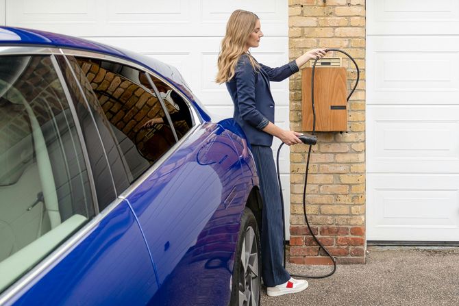 Woman plugging a charging cable into a luxury electric vehicle at home.