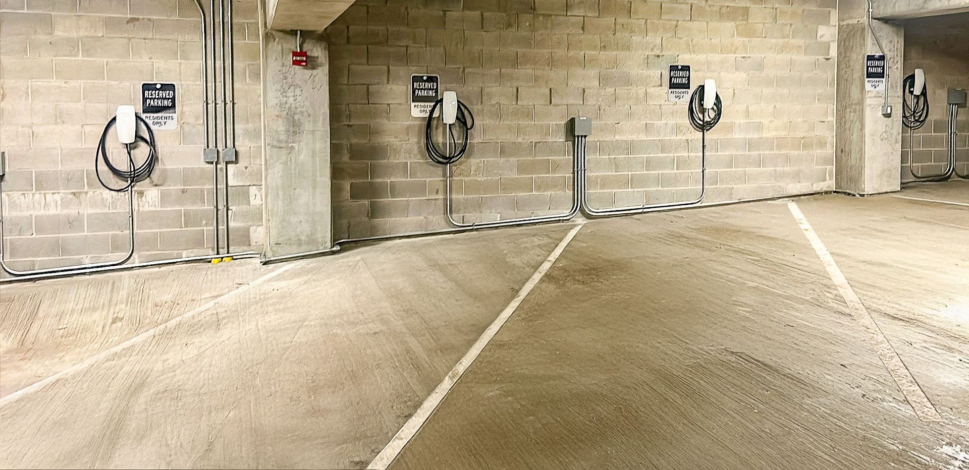 A parking garage with concrete floors and walls and concrete pillars with parking meters on them.
