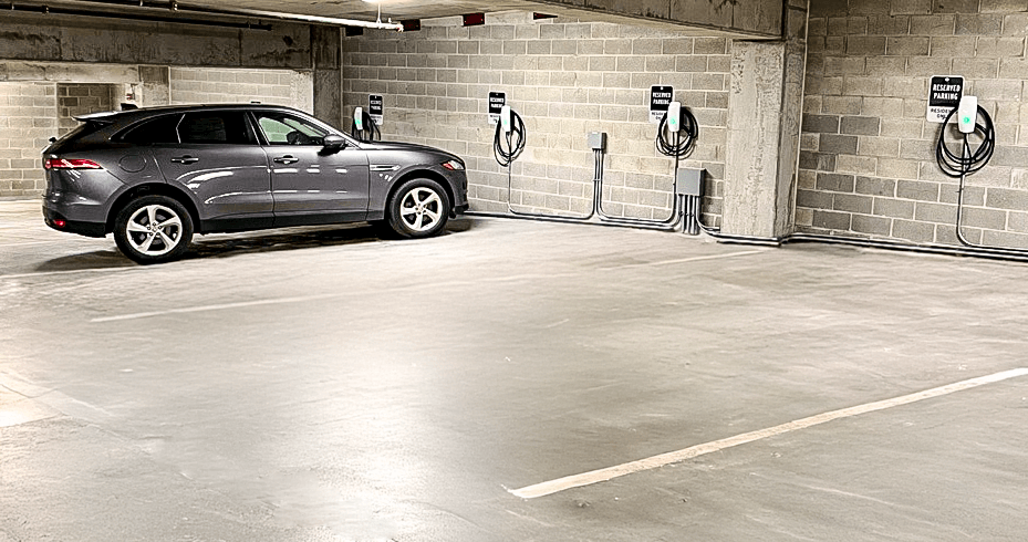 A grey car is parked in a parking garage with four electric vehicle charging stations.