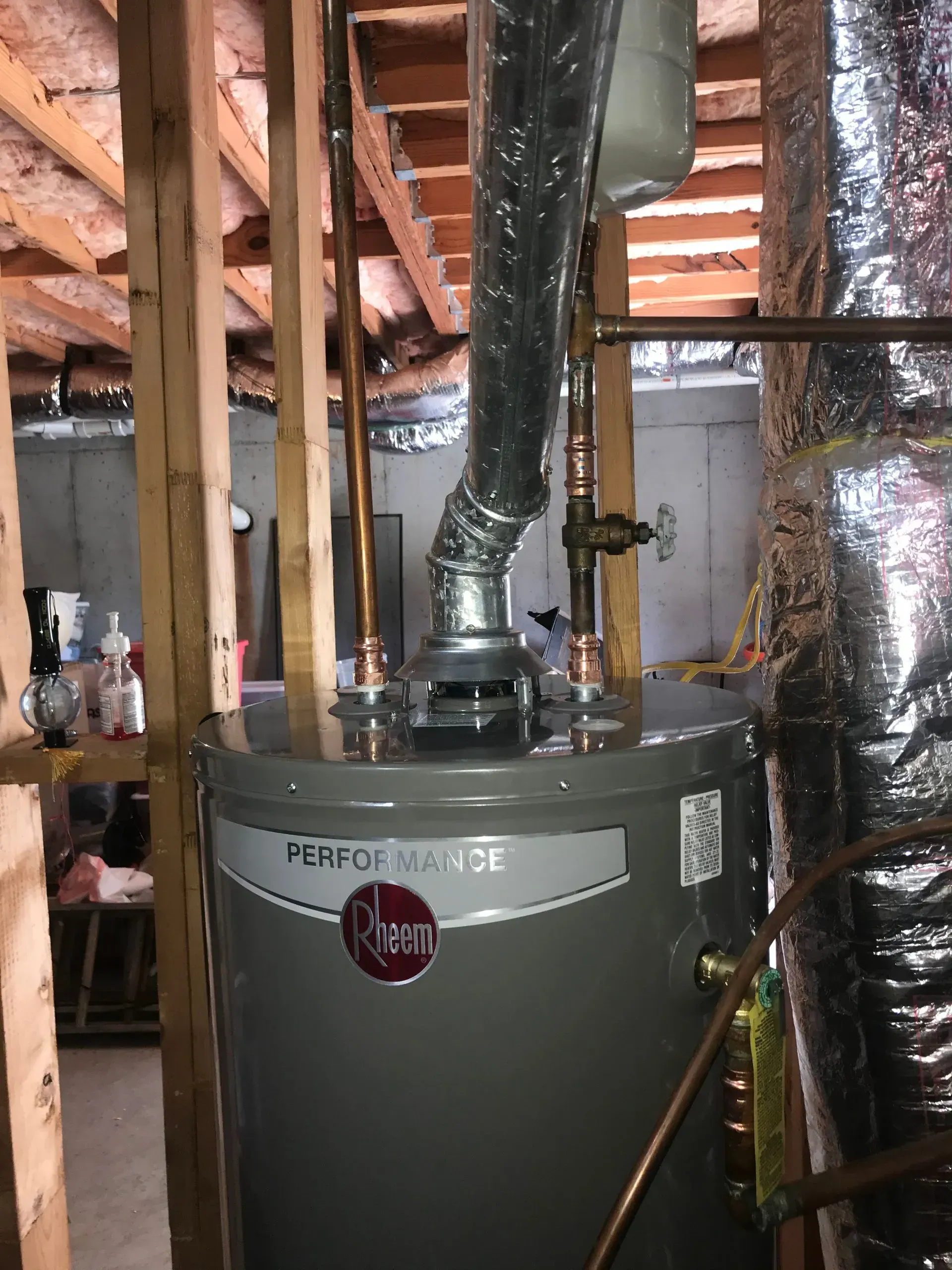 A gray Rheem Performance water heater in a basement with copper pipes and a metal vent pipe.