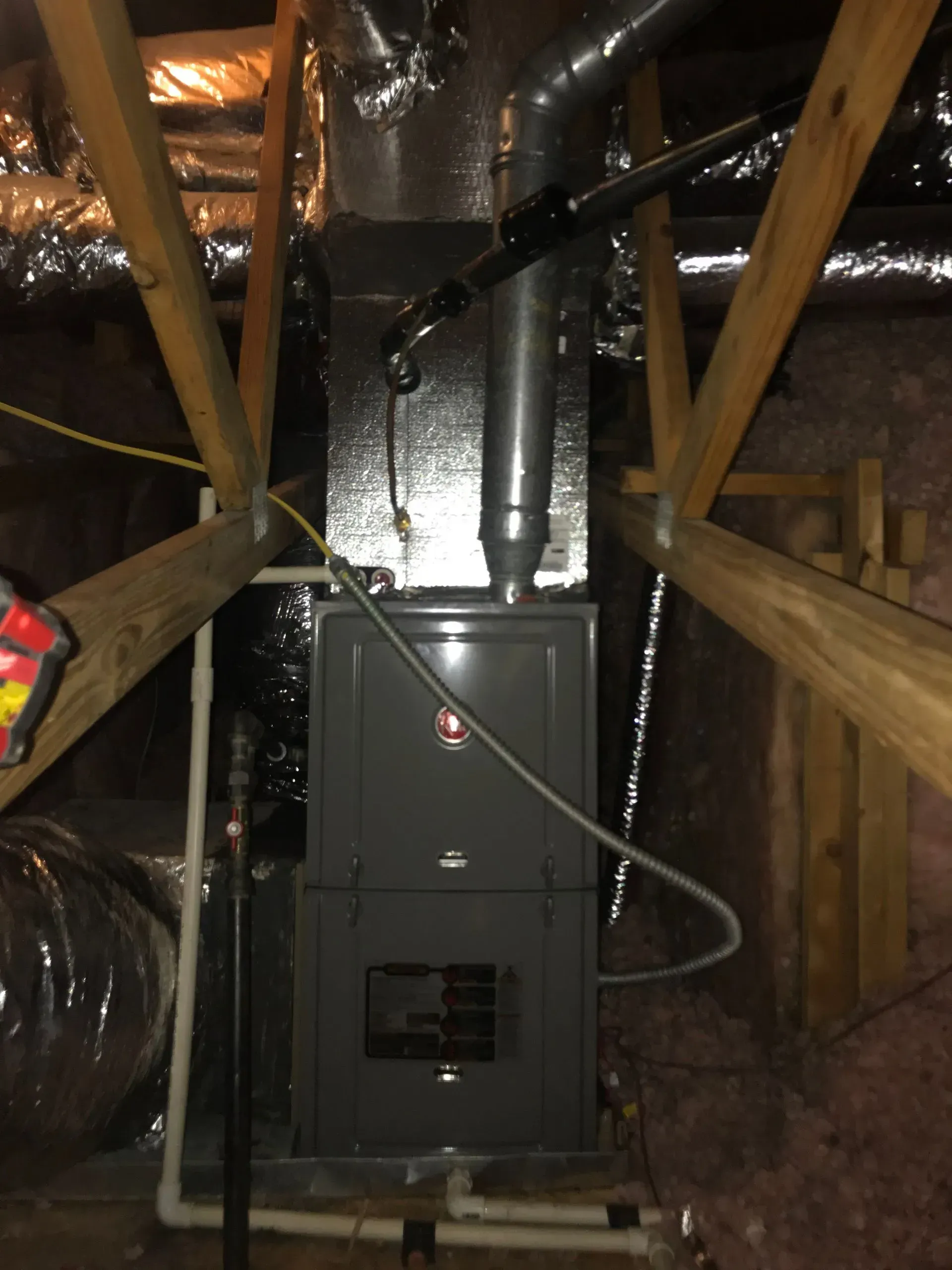 Furnace installed in an attic space, surrounded by wooden beams, ductwork, and insulation.