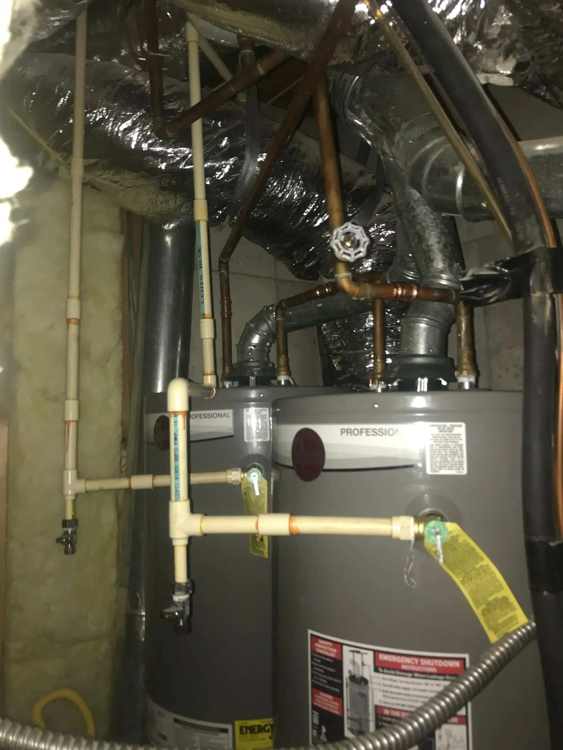 Two gray water heaters with PVC and copper pipes in a utility room.